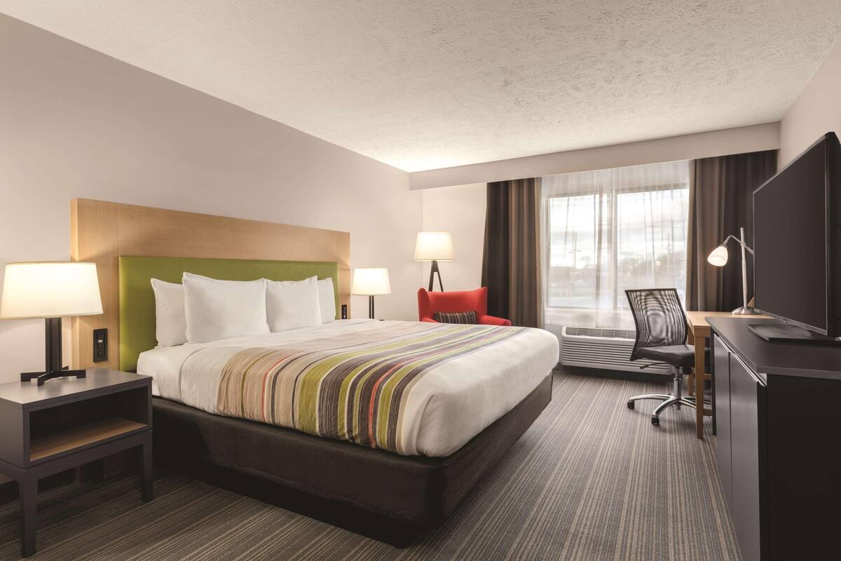 A hotel room with a bed, bedside tables, a desk, a chair, and a television.