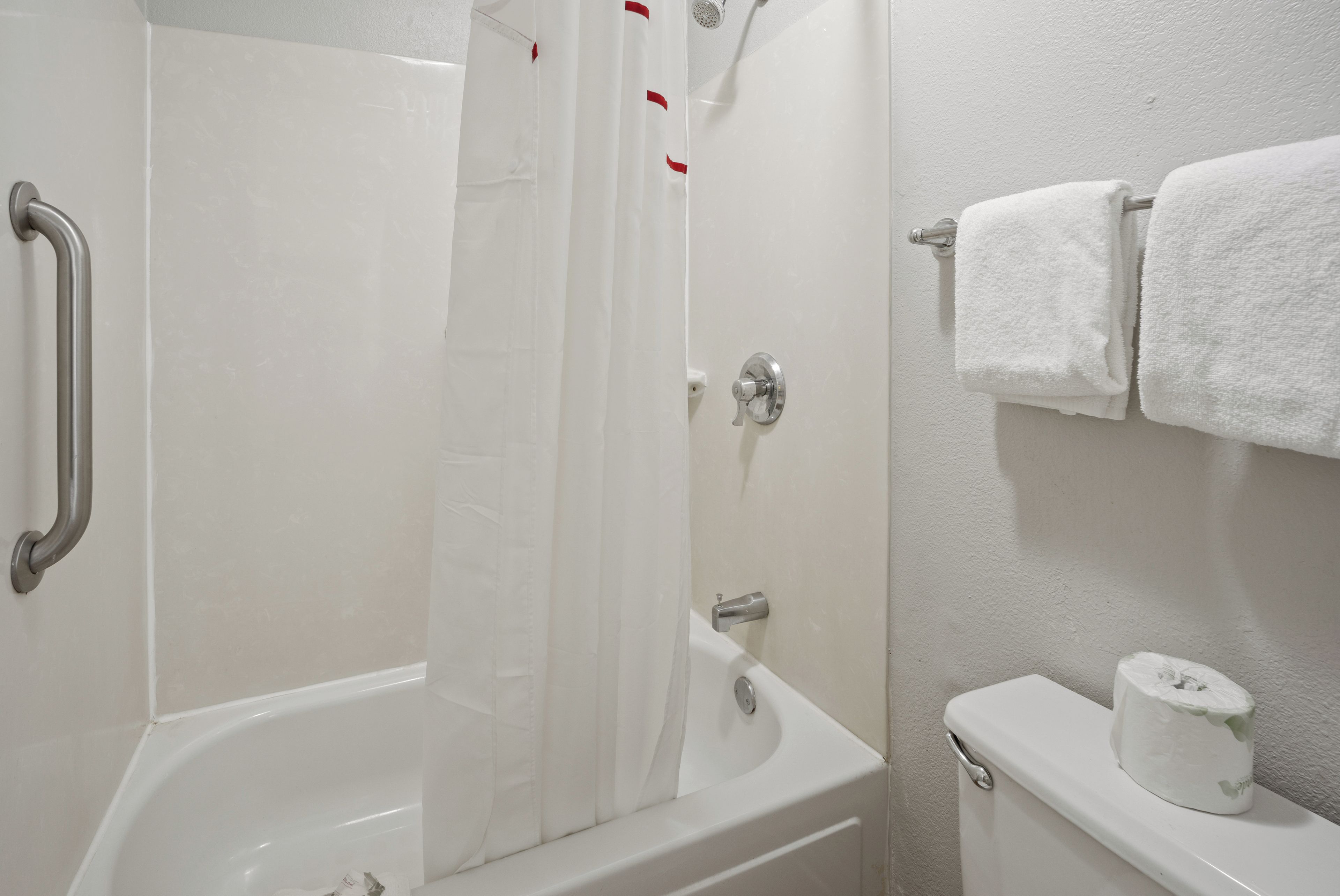 A bathroom with a bathtub, a shower curtain, a toilet, and a towel rack.