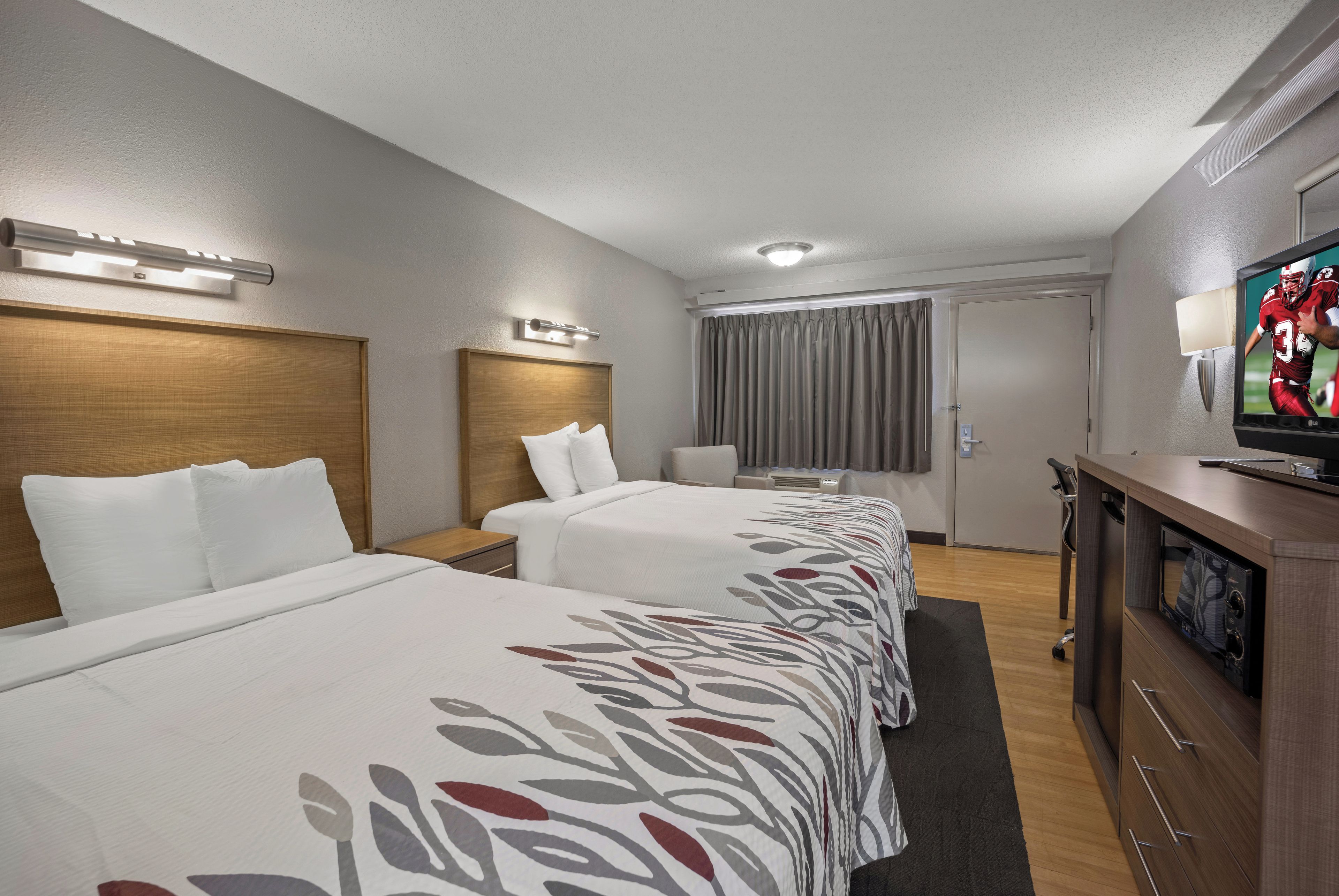 Une chambre d’hôtel avec trois lits, une télévision, un bureau et une fenêtre avec des rideaux.