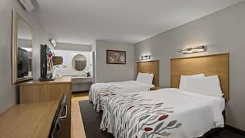 A hotel room with two beds, a desk, a mirror, a television, and a bathroom.