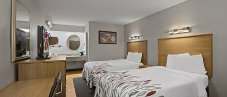 A hotel room with two beds, a desk, a mirror, a television, and a bathroom.