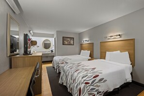 Habitación de hotel con dos camas, un escritorio, un espejo, un televisor y un baño.