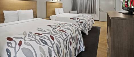 A hotel room with two beds, a desk, and a television.
