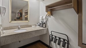 A bathroom with a granite countertop, a sink, a mirror, a towel rack, and a wooden shelf. - Red Roof Inn Greensboro Airport (Greensboro)