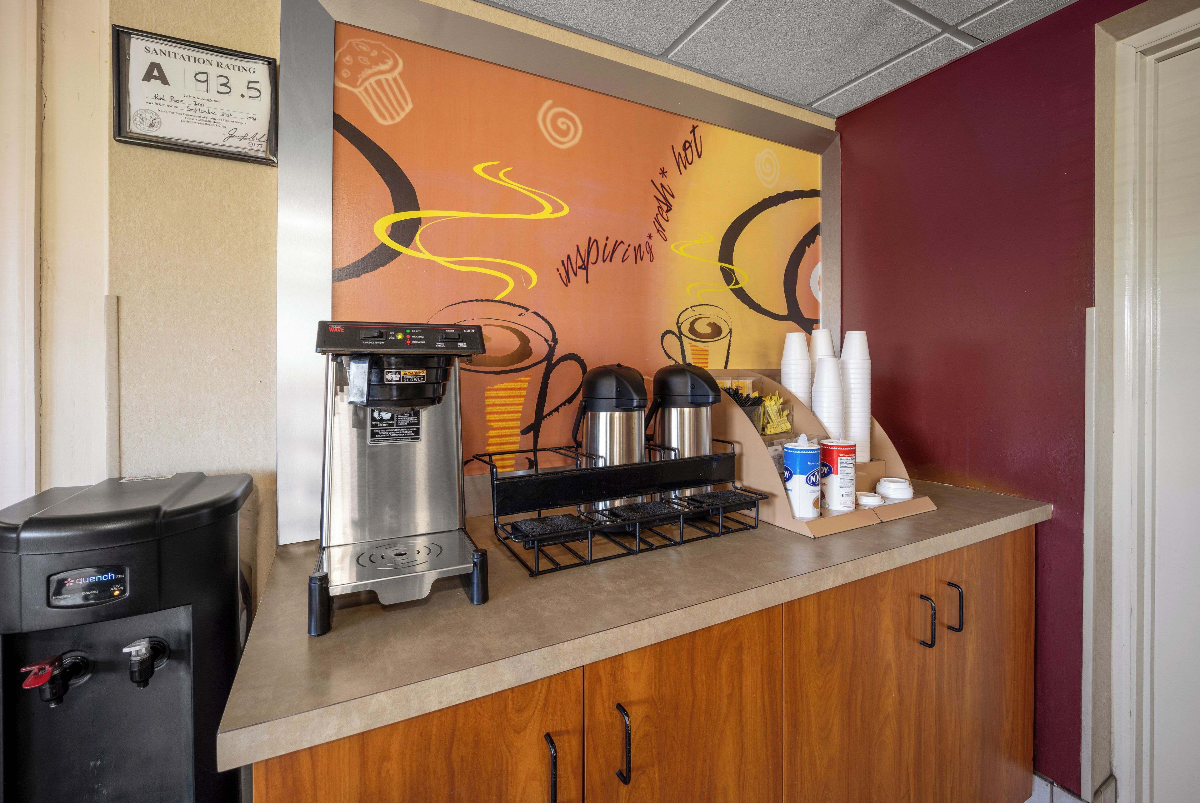 A coffee station with a coffee machine, a grinder, and a coffee urn. There are cups and a box of napkins on the counter.