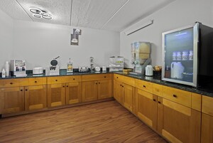 Una cocina con armarios de madera, cafetera, plancha para waffles y refrigerador.