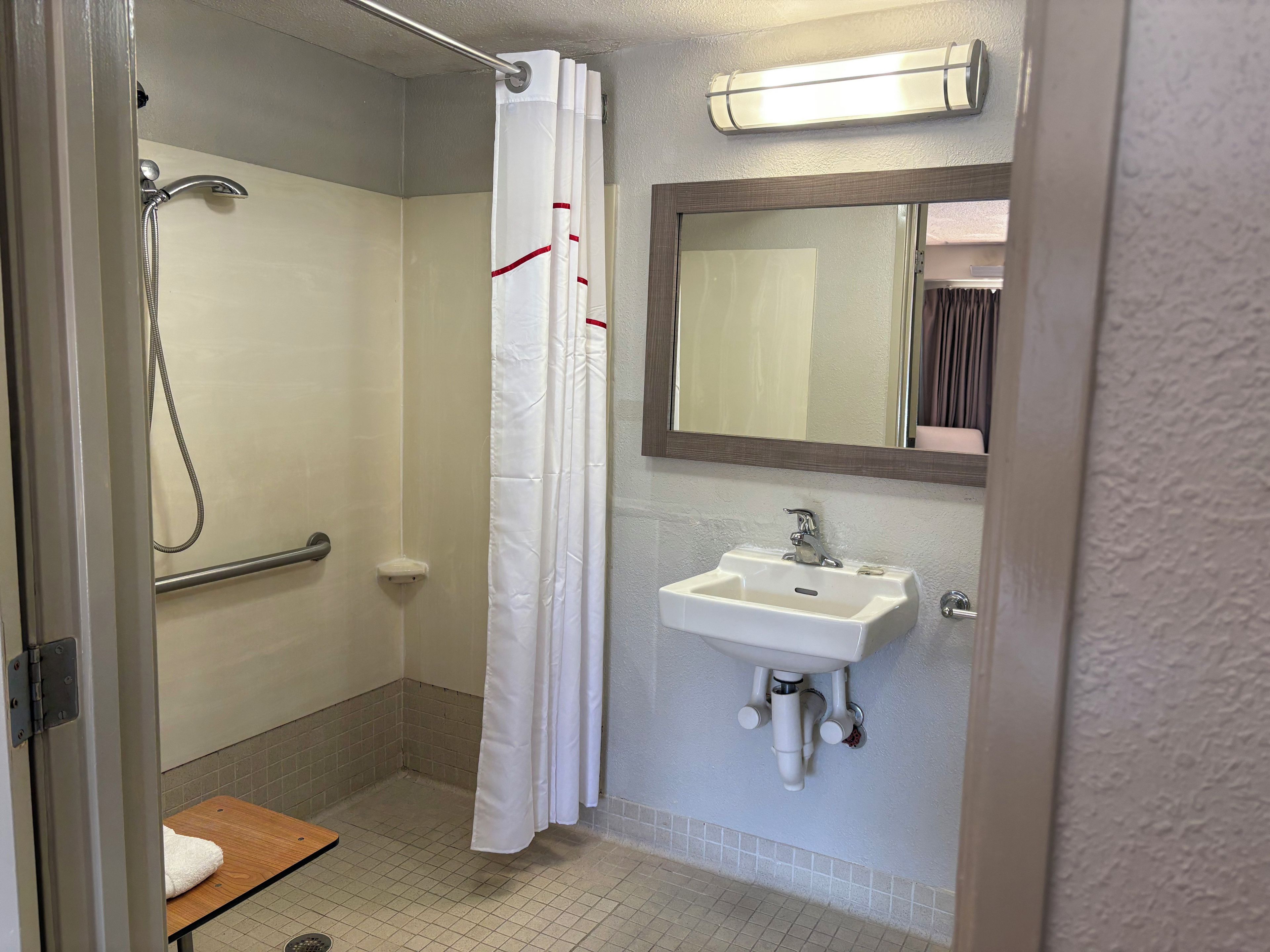 A bathroom with a shower, a sink, a mirror, and a towel rack.