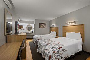 A hotel room with two beds, a desk with a chair, a mirror, a television, and a small bathroom. - Red Roof Inn Greensboro Airport (Greensboro)