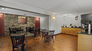 A restaurant with a stone wall, wooden tables, and chairs. - Red Roof Inn Greensboro Airport (Greensboro)