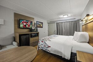 Habitación de hotel con cama, escritorio, televisor, microondas y puerta con cortinas.