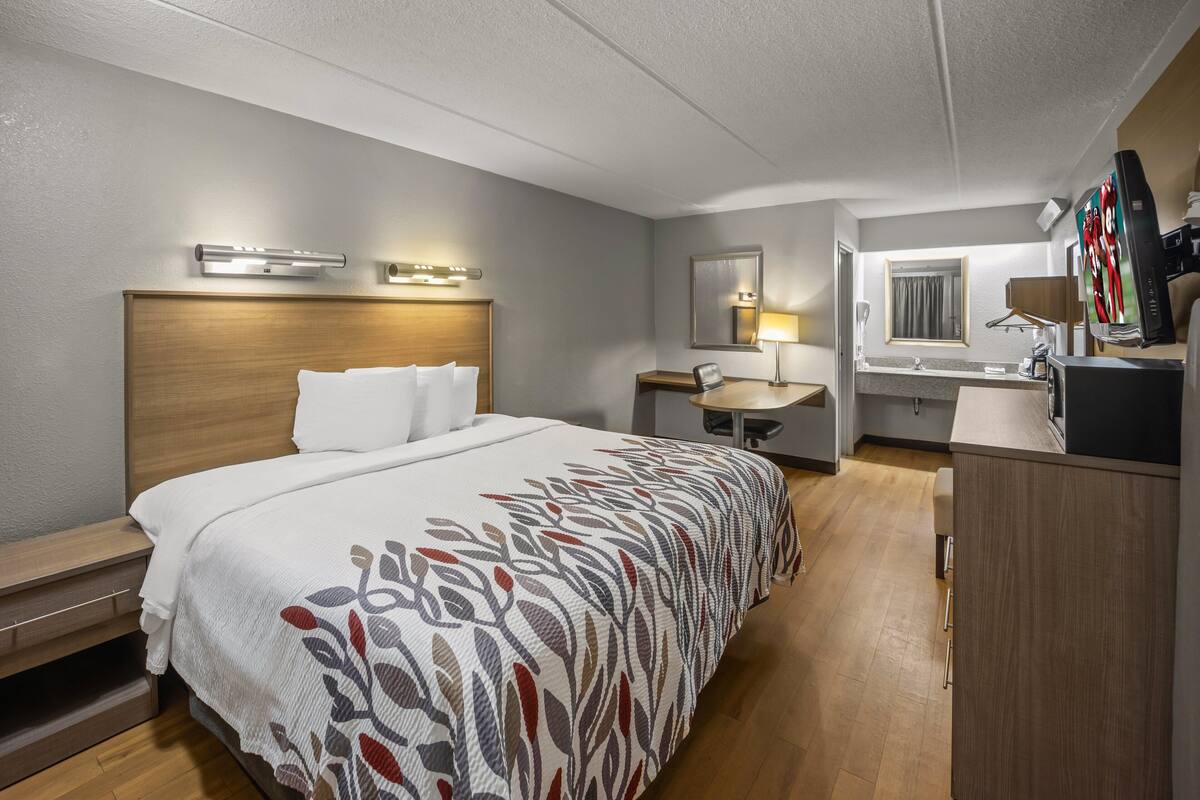 Habitació d'hotel amb un llit gran, una taula de treball, un mirall, un frigorífic i una finestra.