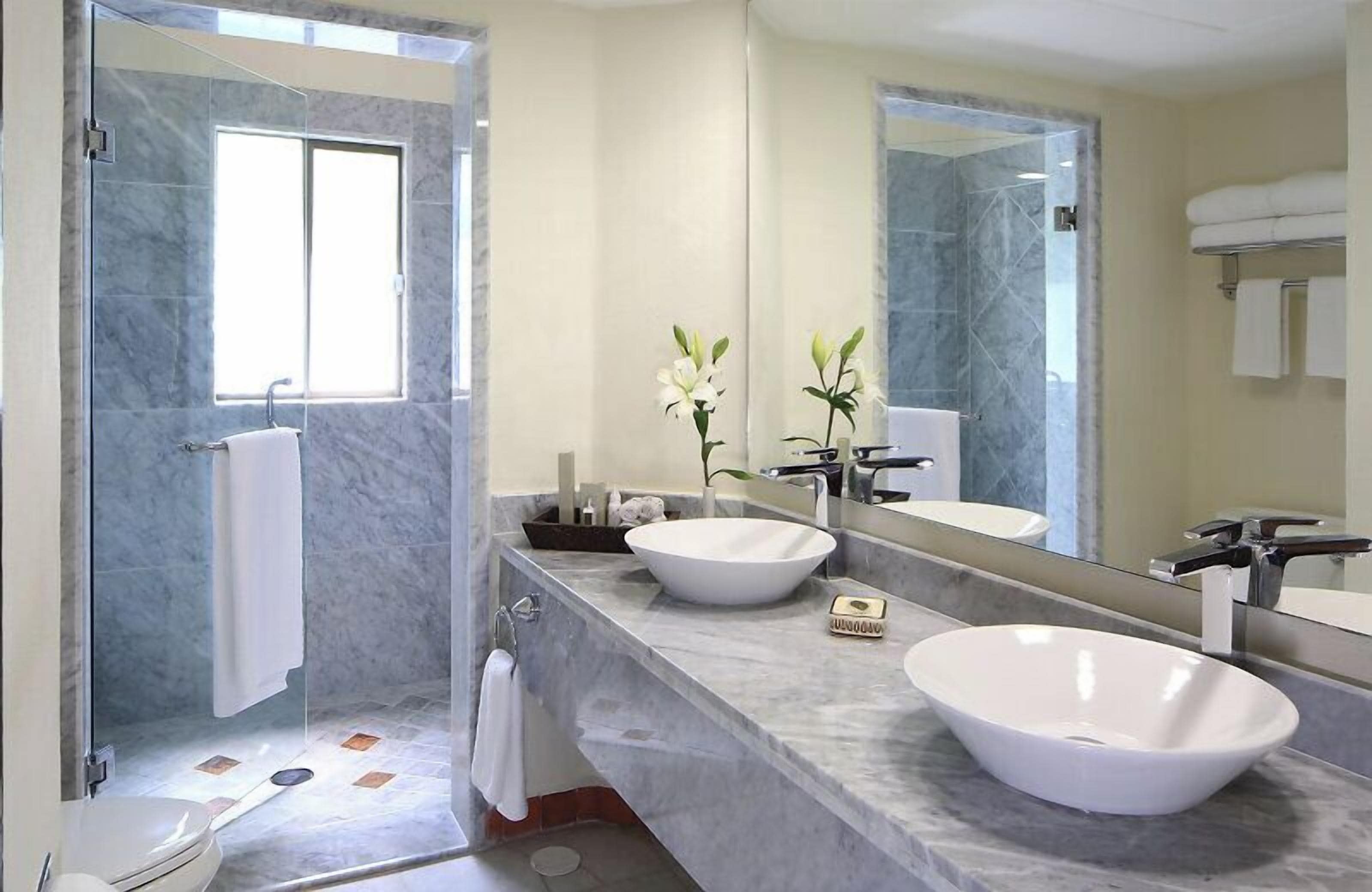 Een moderne badkamer met twee grote witte wasbakken, een douchecabine van glas en een grote spiegel.