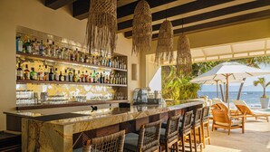 A bar area with a marble countertop, wicker chairs, and a view of the ocean.