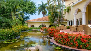 A serene garden with a pond, lush greenery, and outdoor seating.
