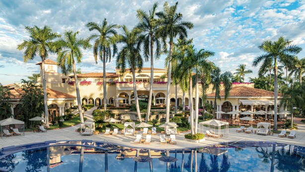 A resort with a large pool, palm trees, and outdoor seating areas.