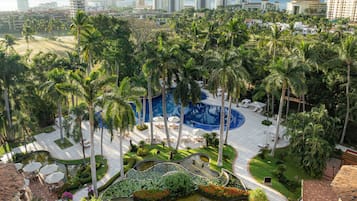 A resort with a swimming pool surrounded by palm trees, a landscaped garden, and a view of the city skyline.