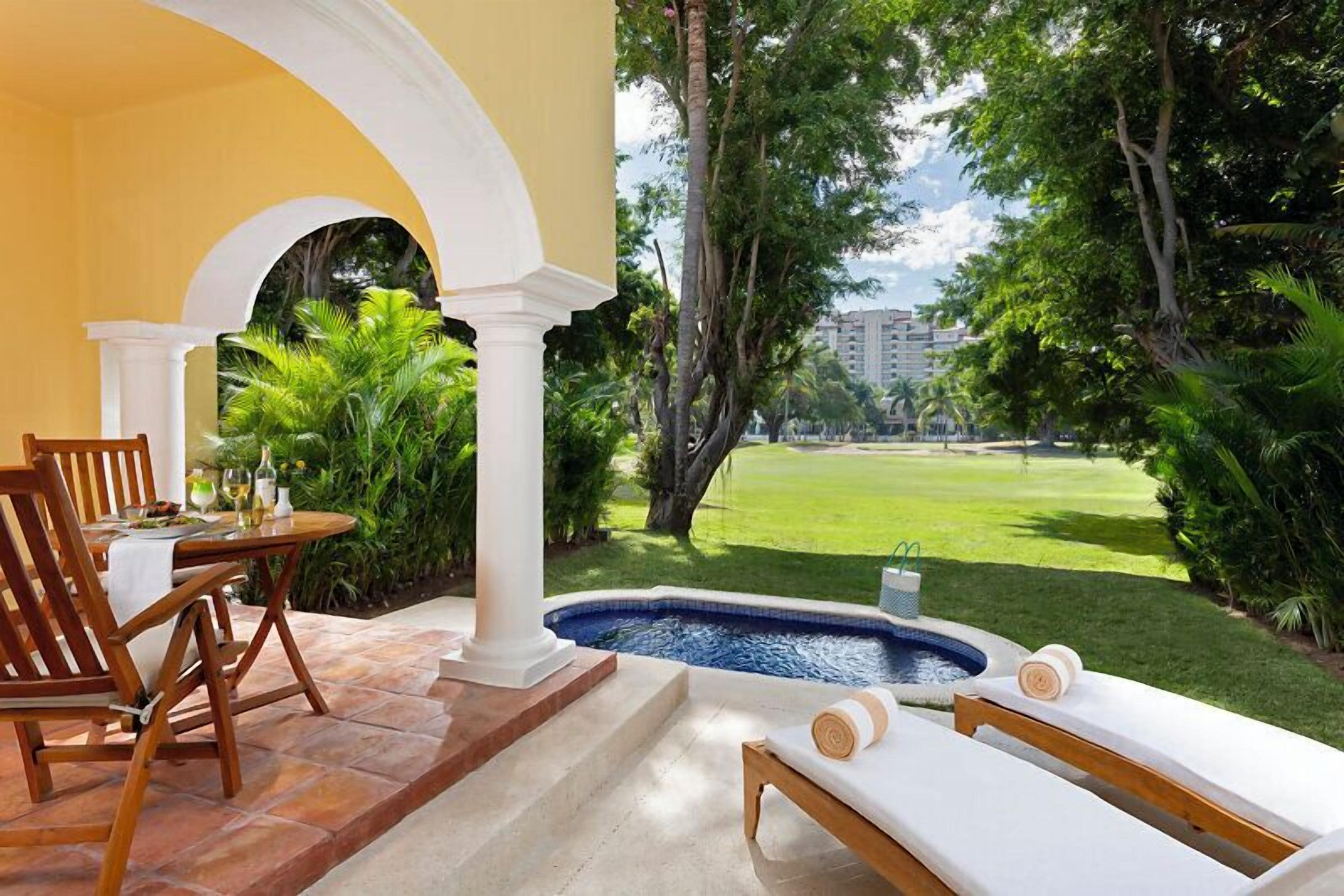 Zona de piscina amb taula i cadires, una cadira relaxant i vista a un camp de golf.
