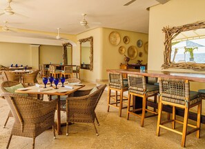 A dining area with wicker furniture, a wooden table, and blue glassware.