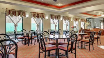 A dining area with tables and chairs, a ceiling fan, and large windows with curtains.