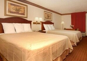 A hotel room with two beds, a wooden headboard, a nightstand with a lamp, and a red curtain.