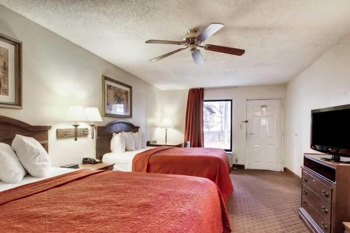 Ein Hotelzimmer mit zwei Betten, einem Deckenventilator, einem Fernseher und einer Tür.