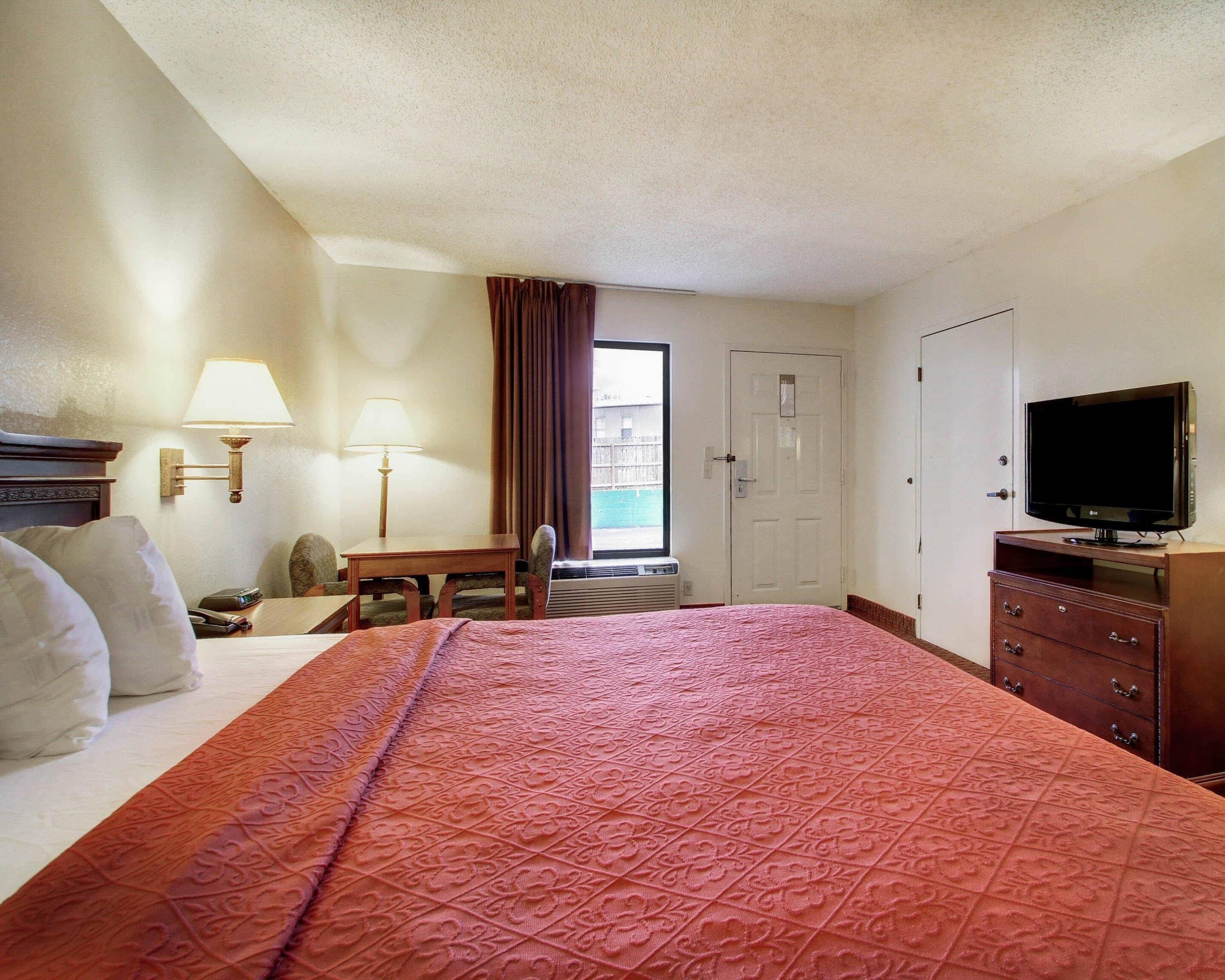 A hotel room with a bed, a desk, a chair, a television, and a door.