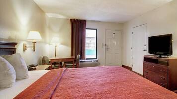 A hotel room with a bed, a desk, a chair, a television, and a door.