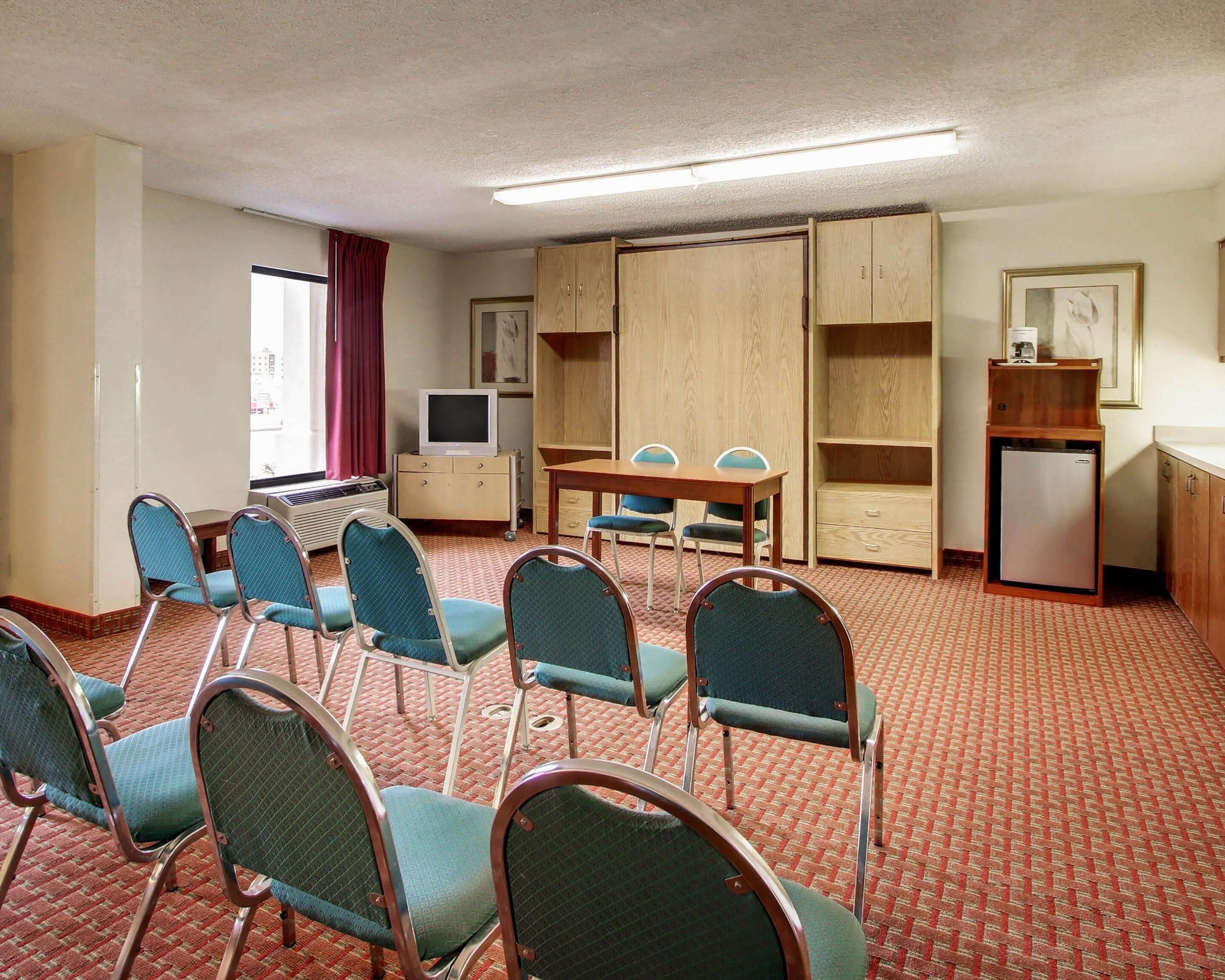 A hotel room with a bed, a desk, a chair, a television, a small refrigerator, and a window with curtains.