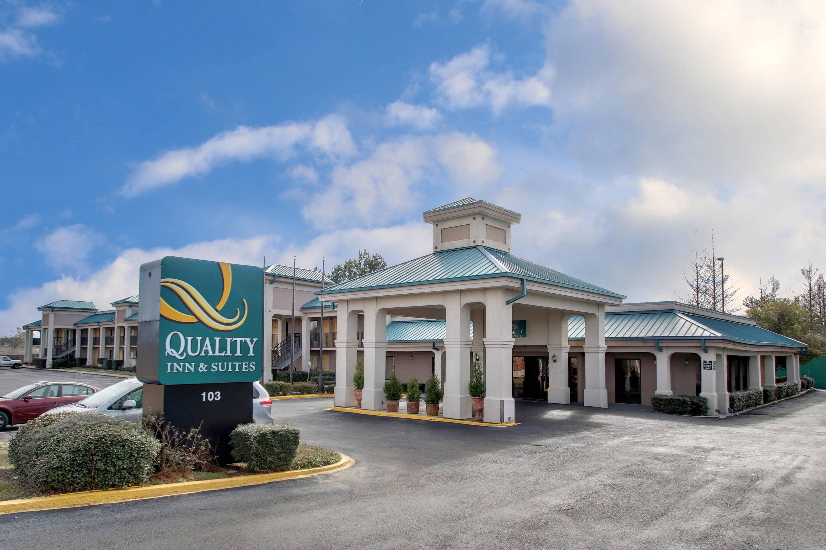 A hotel with a sign reading 'Quality Inn & Suites 103,' a covered entrance, and a parking lot.
