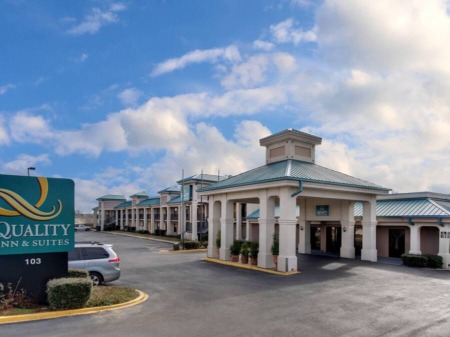 Un hôtel avec une enseigne indiquant « Quality Inn & Suites 103 », doté d’un espace extérieur couvert avec des colonnes et d’un parking.