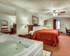 A hotel room with a large bed, a sitting area with a chair, a desk, a television, a ceiling fan, and a bathtub. - Quality Inn & Suites Clinton - Jackson West (Clinton)