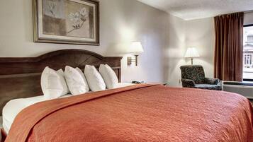 A hotel room with a large bed, two wall-mounted lamps, a chair, and a painting on the wall.