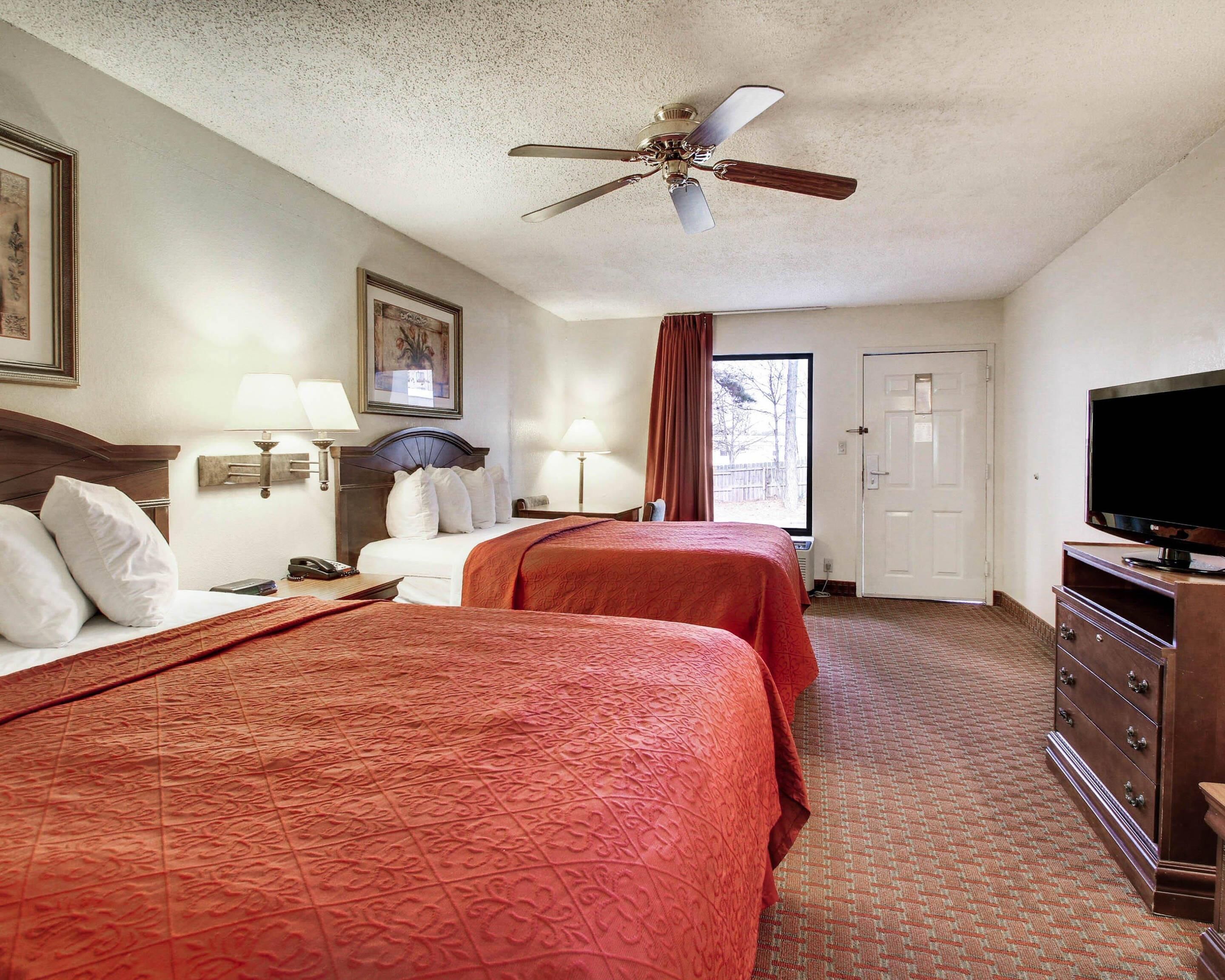 A hotel room with two beds, a ceiling fan, a television, and a door.
