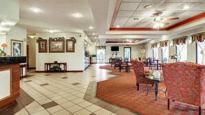 A hotel lobby with a reception desk, dining area with chairs and tables, and a patterned carpet.