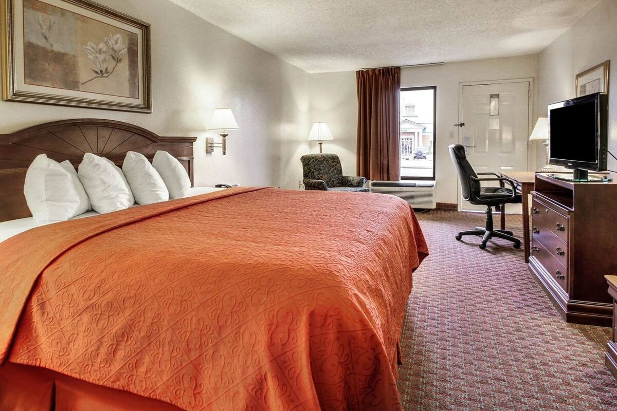 A hotel room with a large bed, a desk with a chair, a television, and a window with curtains.