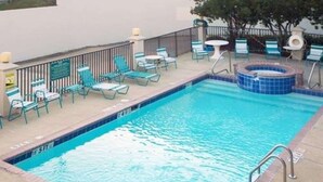 A rectangular pool with a hot tub, surrounded by lounge chairs and a small table.