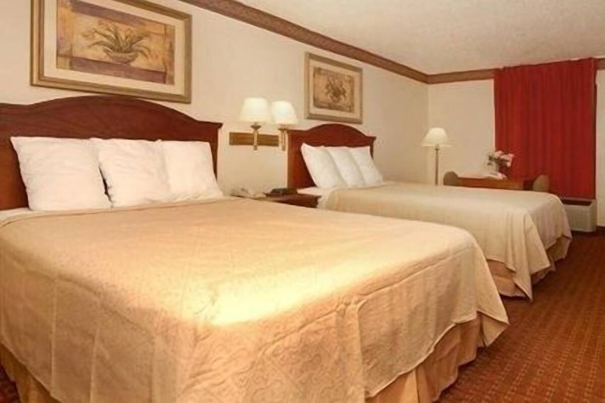 A hotel room with two beds, a nightstand with a lamp, and a painting on the wall.