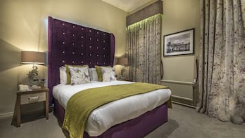 A bedroom with a large bed, two bedside tables, a nightstand, a lamp, a framed picture on the wall, and a window with curtains.