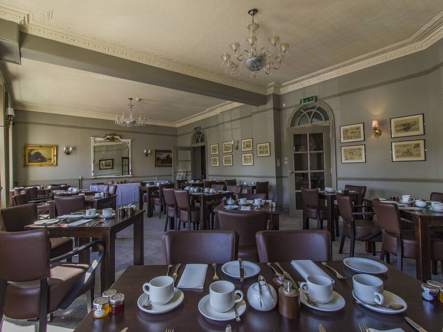 A formal dining room with multiple tables set for service, elegant chandeliers, and framed artwork on the walls.