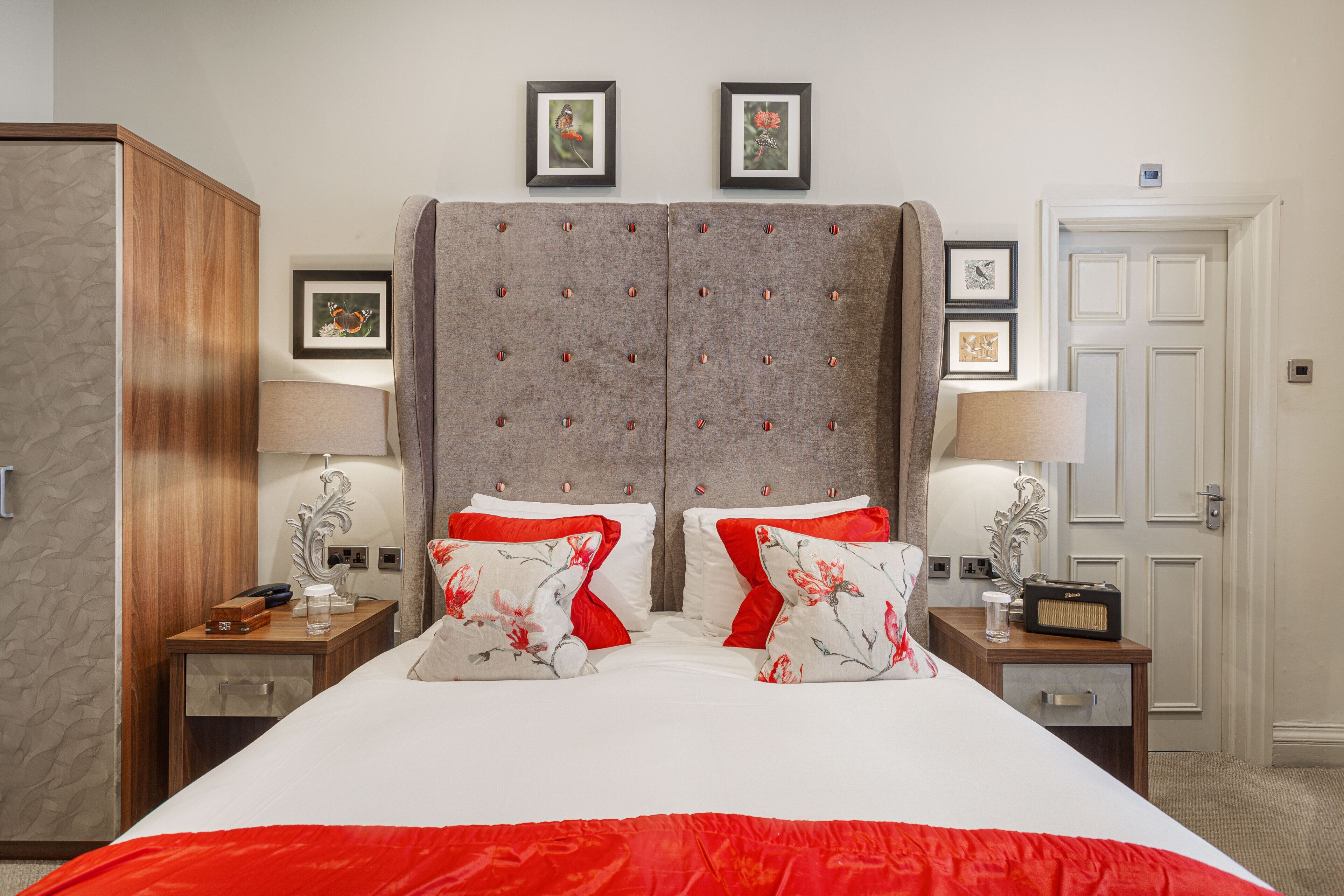 A hotel room with a large bed, two nightstands, a wardrobe, and framed pictures on the wall.