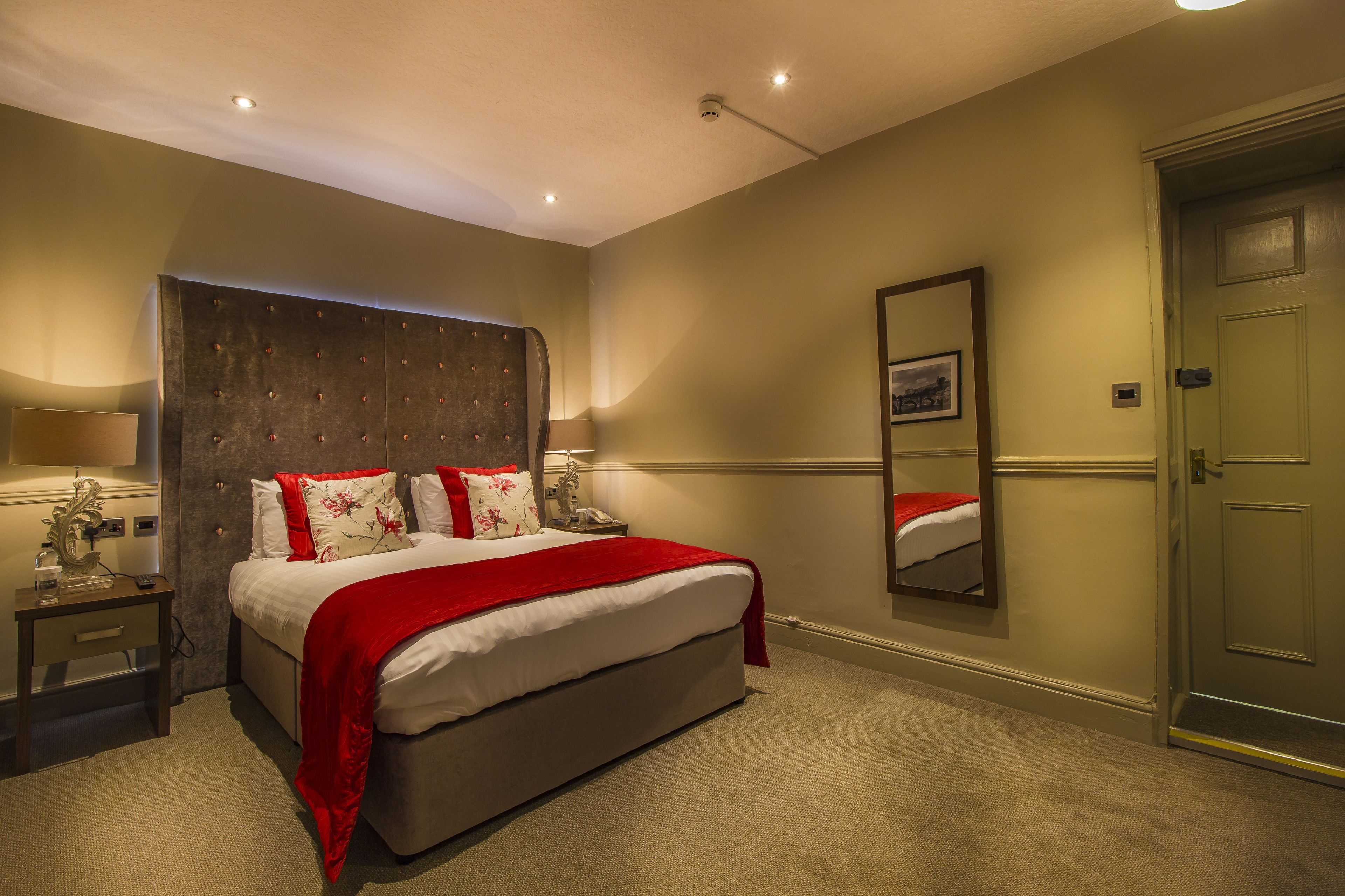 Une chambre d’hôtel avec un grand lit, une table de chevet, une commode, un miroir et une porte.