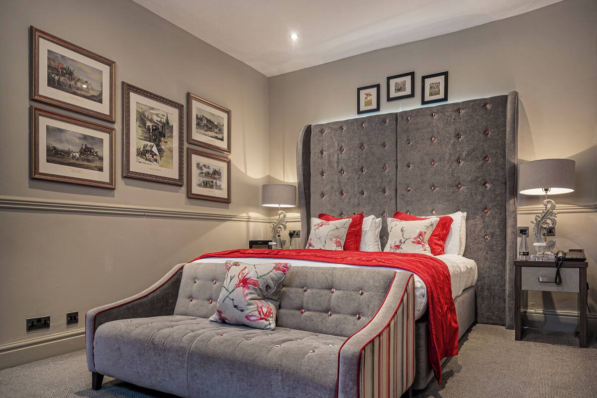 A bedroom with a bed, a sofa, a nightstand, a lamp, and framed pictures on the wall.