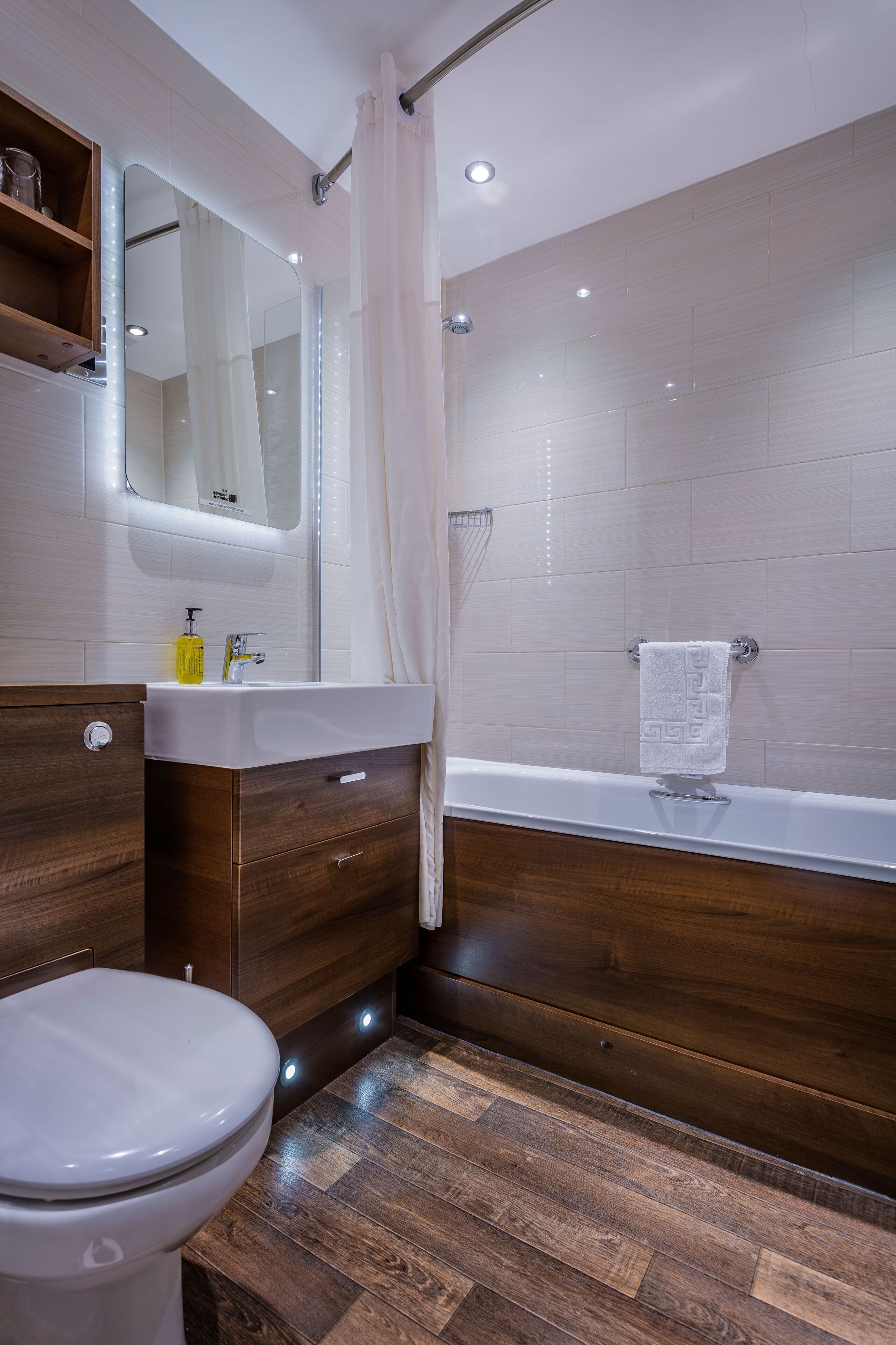 A modern bathroom with a wooden vanity, a white sink, a mirror, a shower, and a toilet.