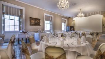 A banquet hall with round tables set for a formal event, featuring white tablecloths and chairs with gold sashes.