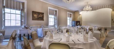 A banquet hall with round tables set for a formal event, featuring white tablecloths and chairs with gold sashes.