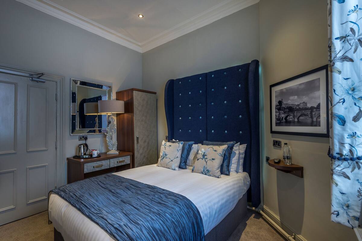 A bedroom with a large bed, a wardrobe, a mirror, a bedside table, and a framed picture on the wall.