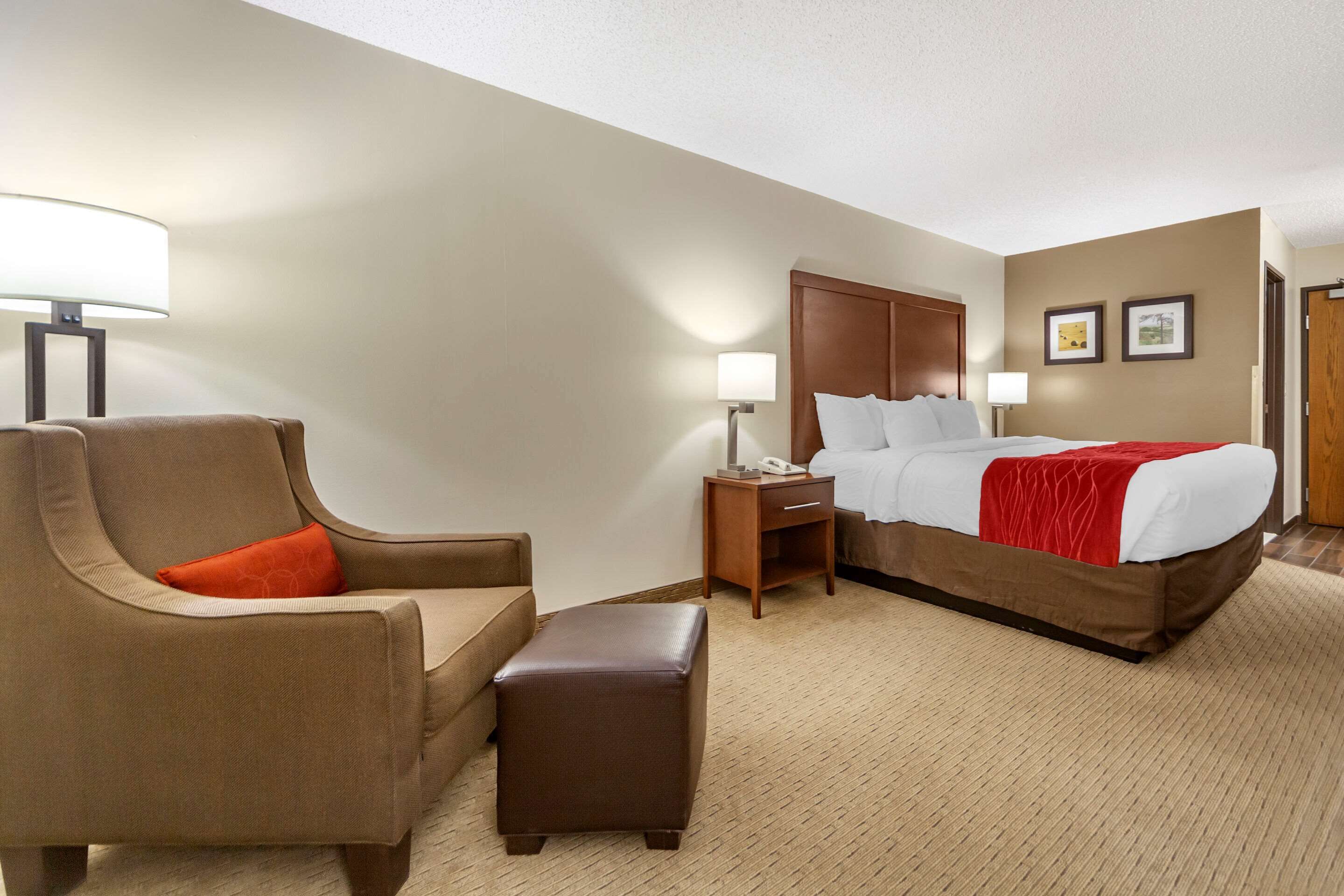 Una habitación de hotel con cama, una silla, una mesita de noche, una lámpara y una pequeña mesa.