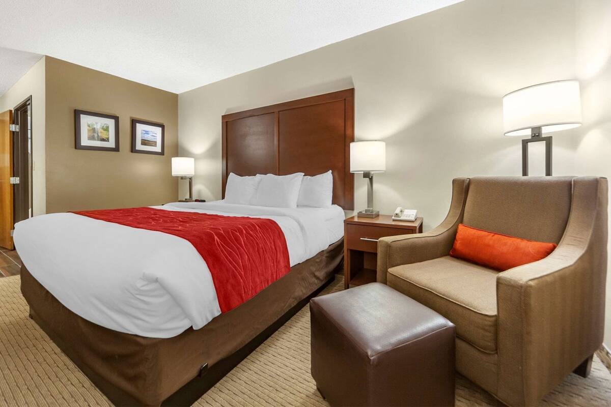 A hotel room with a large bed, two bedside tables, a chair, and a small ottoman.