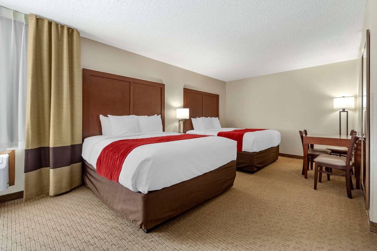 A hotel room with two beds, a desk, and a chair.