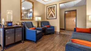 A hotel lobby with a reception desk, two armchairs with orange cushions, a sofa with orange cushions, a large mirror, and a framed abstract artwork on the wall. - Comfort Inn Valentine (Valentine)